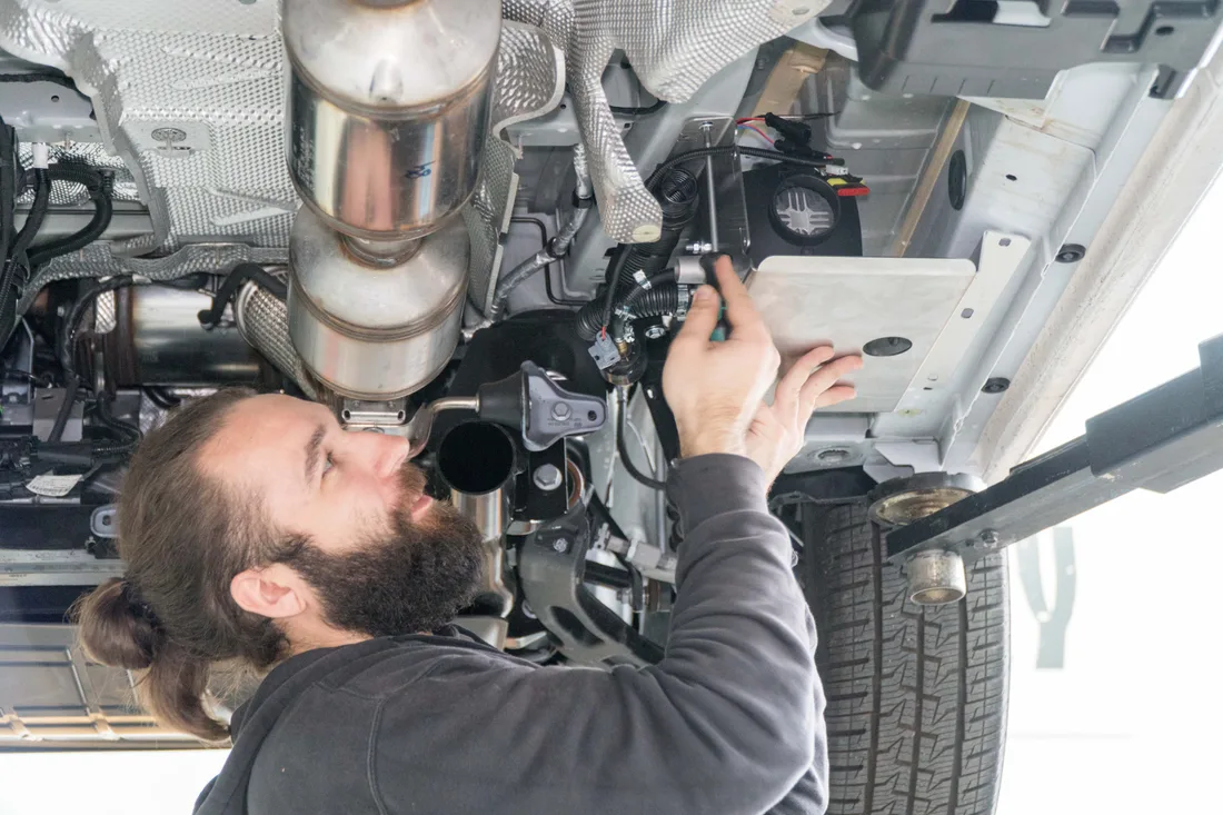 Monteur beim Einbau einer Standheizung unter einem Campingbus